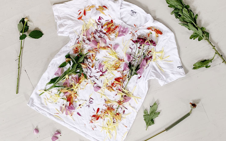 White t-shirt laid out with flowers and greens laying on it. 